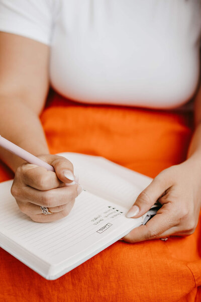 Woman writing in journal with white shirt and orange skirt