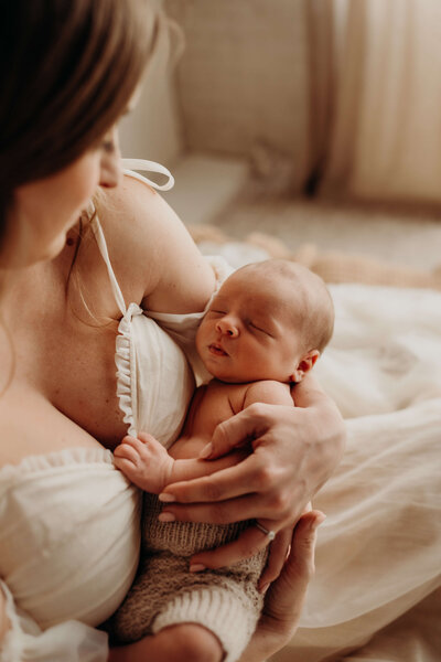 newborn baby boy holds onto mom while he sleeps