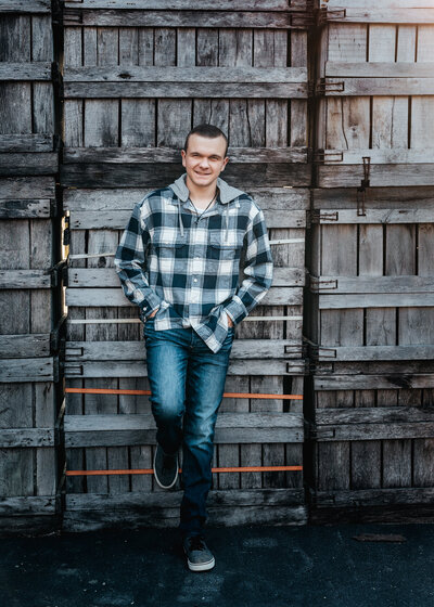 High school senior guy in plaid shirt posing in front of a fence for senior portraits in Greeley Park Nashua NH