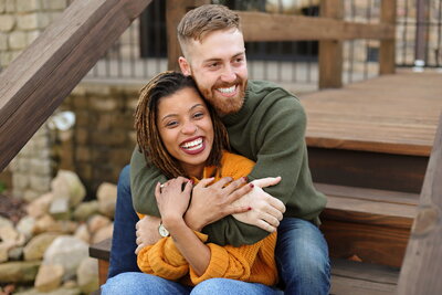 Engagement couple laughing and embracing while sitting on the steps outside