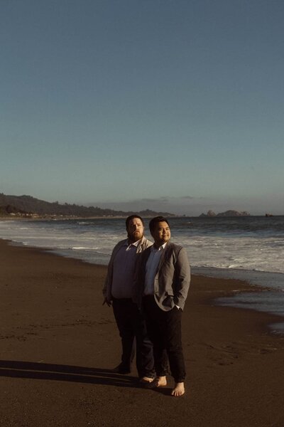 Two grooms watching the sunset after their Oregon Coast elopement