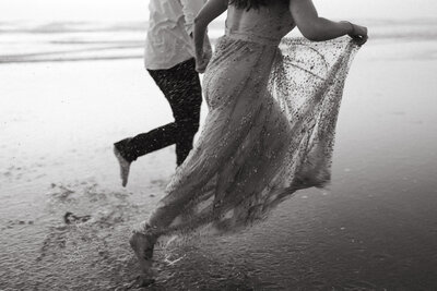 bride and groom run through sand