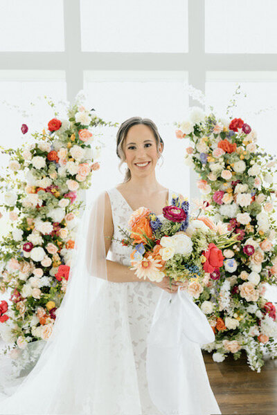 Bright colored bridal bouquet held by bride in front of floral arch at The Grand at Willow Springs Wedding Venue