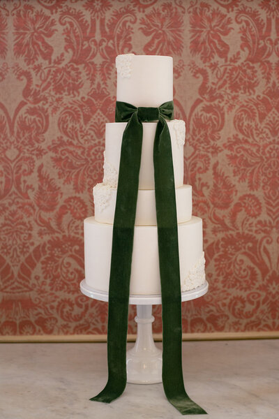Elegant white wedding cake with sculptural details and a green velvet bow at Newington House