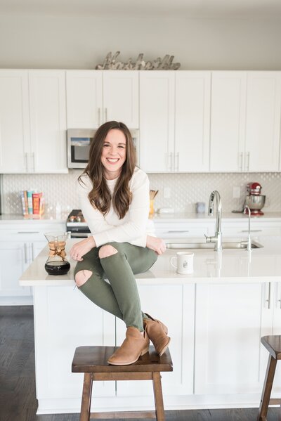 Casual headshot of a woman sitting on the kitchen counter with a Chemex of coffee next to her
