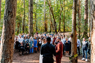 a couple in the middle of the woods surrounded by their people getting married.