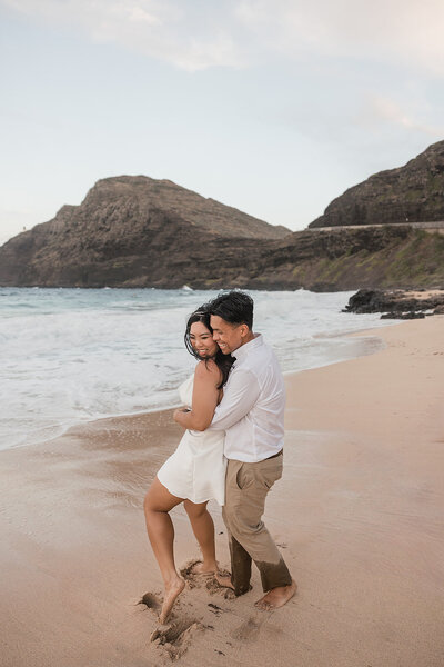 couple hugging on beach with ocean waves and sand