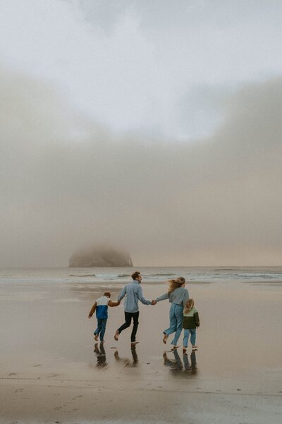 Family running hand in hand along the oregon coast while having their photo taken