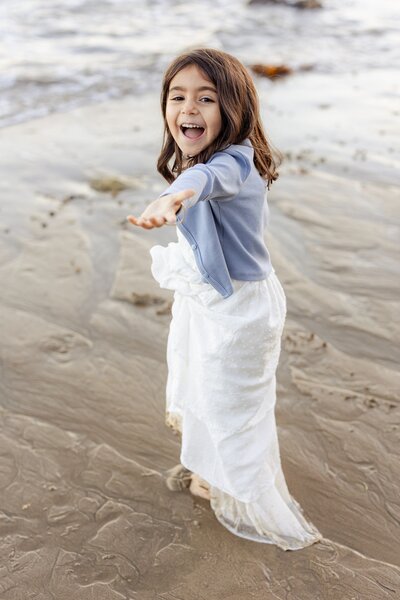 portrait of girl holding her hand out towards the camera while standing in wet sand at Malibu beach