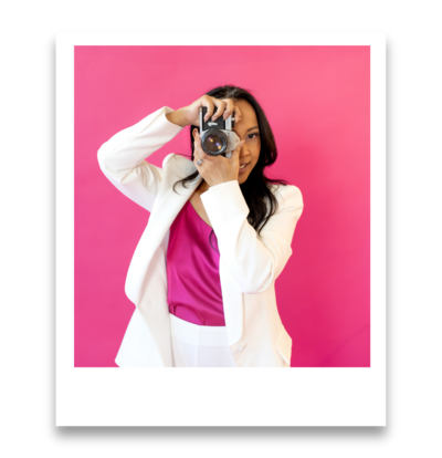 Elegant Dallas brand photographer posing with an analogue camera in a white outfit against a vibrant pink studio background in Dallas, TX
