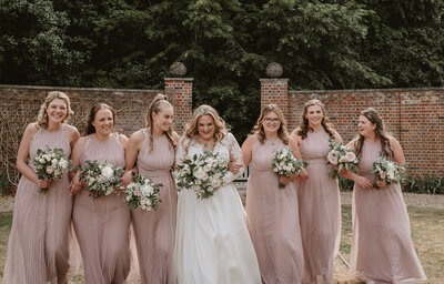 bridesmaids walking with bride laughing and linking arms wearing pink and holding flowers