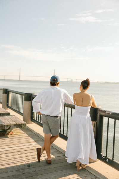 Couple standing along a Charleston waterfront pier at sunset during a relaxed couples photography session.