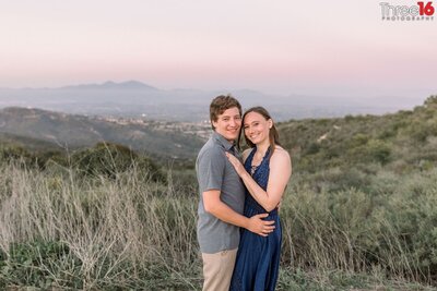 Engaged couple cuddle up for engagement photos on a trail in the Top of the World engagement location in Laguna Beach