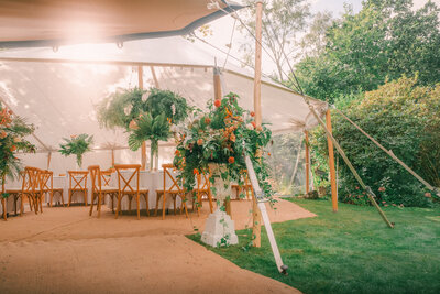 Bride and Groom exchanging vows under outdoor wedding pergola at Eden Barn Cumbria Lake District with flower arch flower installation apricot flowers pampas eucalyptus