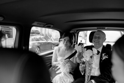 Bride in wedding car holding bouquet, smiling ahead of ceremony.