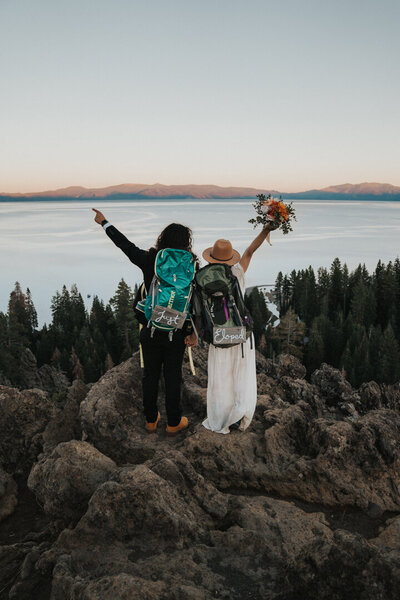 Bride and groom standing on a rock overlooking Lake Tahoe wearing backpacks with just eloped signed by California elopement photographer Kasey Mantiply