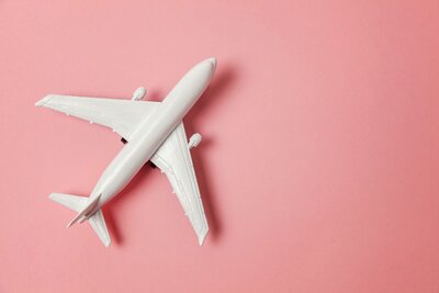 A white toy airplane sits on top of a solid pink background .