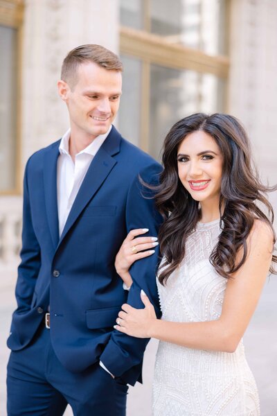 Woman in white dress holding onto the arm of her fiance who is wearing a blue suit for their photos by Winterlyn Stebner, an engagement photographer in Chicago