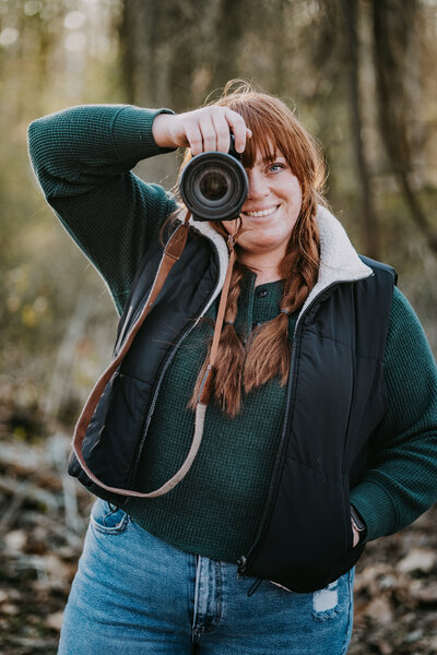 Smiling Savannah holding her camera up, about to take a picture, with a warm sun glow in the background.