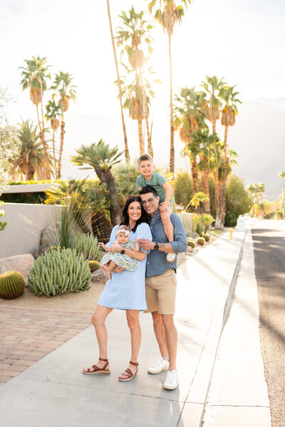 Young family standing on sidewalk in front of Palm trees at sunset. 