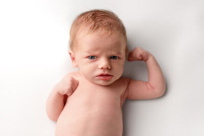 A striking personality portrait of a newborn flexing with confidence—captured in studio lighting to highlight strength and character.