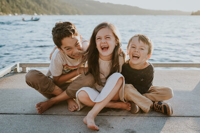 Three young siblings laugh as they sit on Coeur d'Alene Lake dock