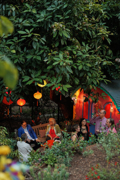 Colorful lounge with hanging Vietnamese lanterns in a big beautiful tree next to a painted wagon.
