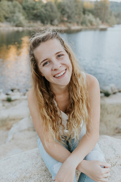 Laura sitting down and smiling at the camera in front of a lake in California.