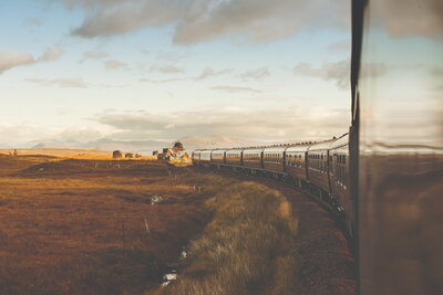 A luxury train glides through the scenic countryside at golden hour, reflecting the warm hues of the landscape. Experience bespoke rail journeys with curated itineraries, private carriages, and high-touch service with Nadia Forte Travel & Events.