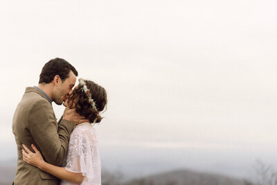 Cinematic image of the couple sharing a kiss on a mountain ridge at golden hour, captured in a nostalgic film-inspired wedding photography style.

