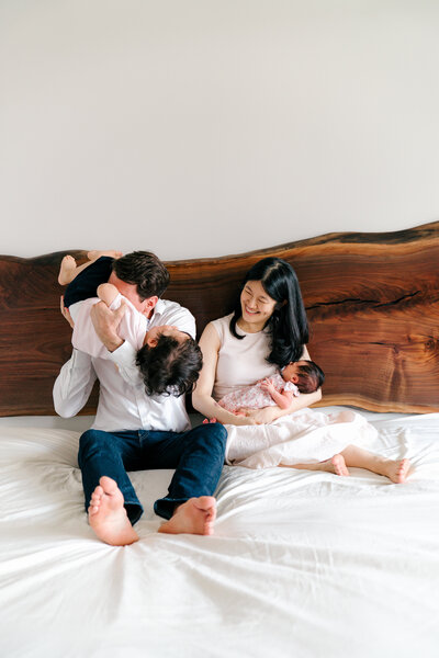 family plays on the bed with their son and newborn baby