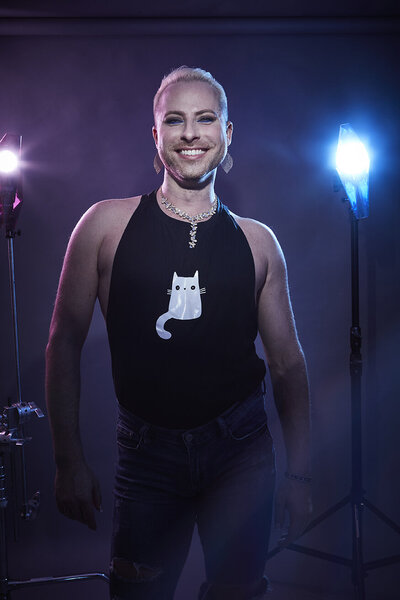 Vibrant studio portrait of Dain August in a black outfit, smiling confidently under dramatic lighting, captured by Ylva Erevall.
