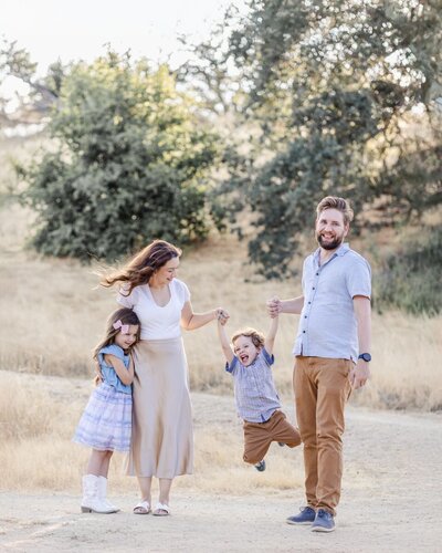Family of four with parents and two children playfully pose during San Jose family photoshoot, with the parents swinging the toddler boy 