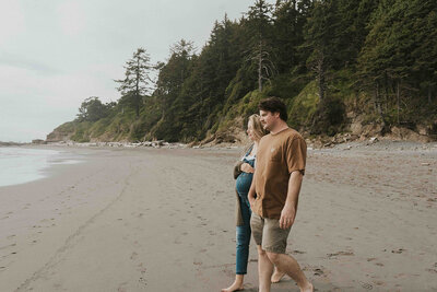 Pregnant person and partner walks towards water at rocky Washington beach