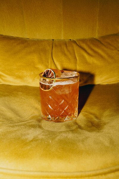 Orange cocktail sitting on a yellow velvet couch
