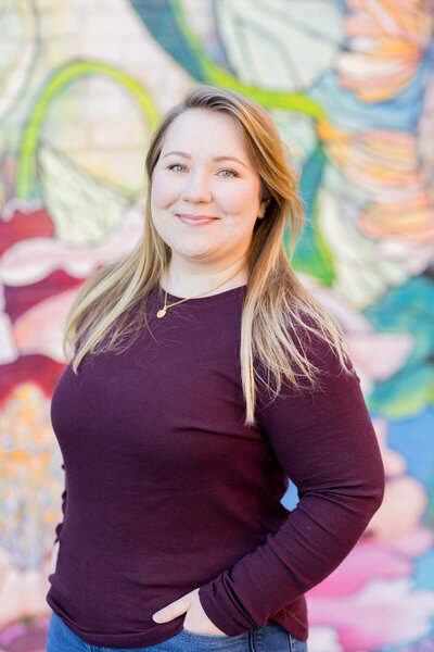 Professional branding portrait of a woman in a burgundy sweater posing in front of a colorful mural in Columbia, SC. Her confident expression and natural lighting create a warm, approachable headshot perfect for business and personal branding photography.