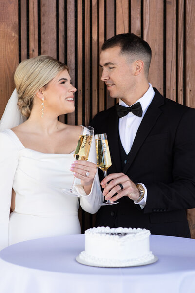 An Austin-based wedding photographer captures the magical moment of a bride and groom toasting with champagne glasses in front of an exquisite cake.