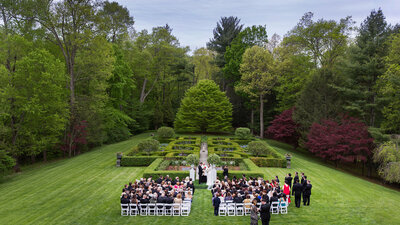Outdoor wedding ceremony with guests seated in front of a lush, landscaped garden
