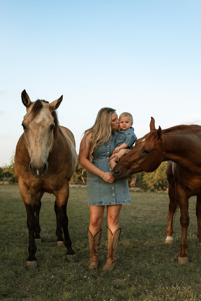 mom holding baby next to horses