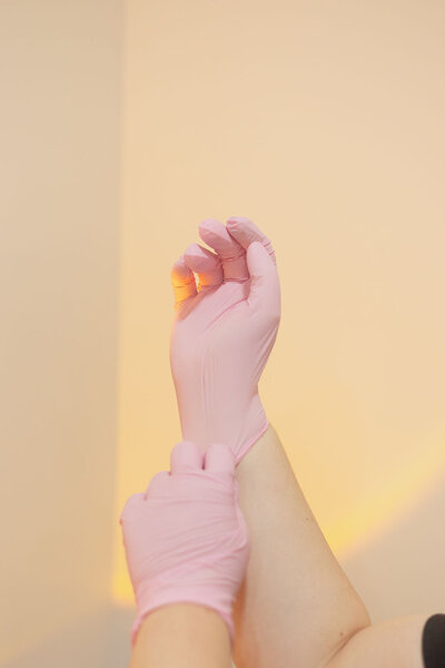 Macayla Hopper, Licensed esthetician putting on pink gloves during prep for client service