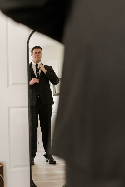 Groom wearing black tuxedo fixing his tie before ceremony | Evalyn & Co. Photography