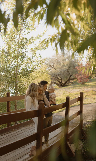 A family of 4 on a bridge, in a park in Rexburg, ID candidly smiling.