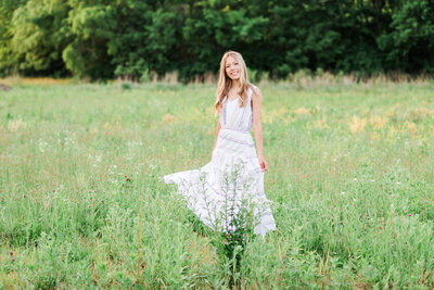 a girl in a white dress smiling while standing next to flowers in a window box