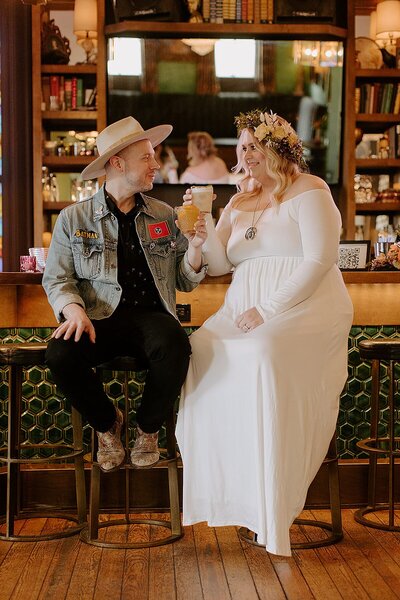 Boho bride with flower crown and groom in a denim jacket and fedora sipping cocktails at trendy Nashville Bar