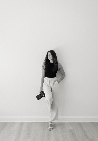 Reilly Erin standing against a white wall holding her camera, embodying her calm and intentional approach to wedding photography.