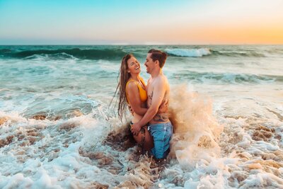 Couple posing in the ocean with waves crashing on them