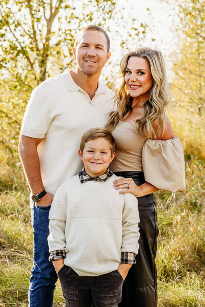 beautiful family of three standing in a golden field in the fall for their family photo session in Door County