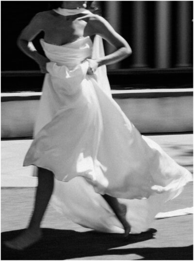 A bride looks over her shoulder while holding up her dress and running barefoot in the street captured by a Wilmington wedding photographer