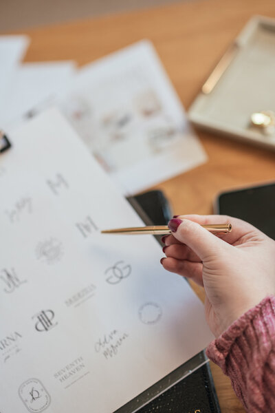Luxury logo designs laid out on a clipboard with pen, showcasing the creative design process.
