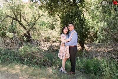 Engaged couple embrace while posing for engagement photos amongst the trees and brush at the James Dilley Greenbelt Preserve in Laguna Beach